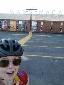 Me, in cycling jersey, sunglasses, and blach bike helmet, standing in front of the Mass MOCA building