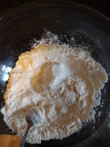 A glass bowl containing flour, salt, and baking powder.