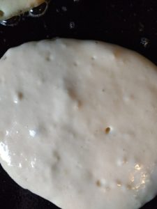 A pancake cooking, the top has small bubbles in it.