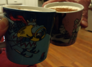 A photo of two mugs of eggnog, sprinkled with nutmeg and cinnamon. The mugs feature a winter scene of characters from the Moomin books.